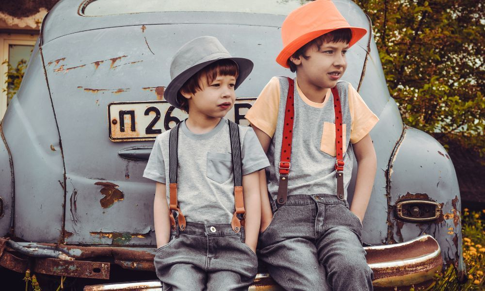 Chłopcy oparci o samochód ubrani w spodnie z szelkami i kapeluszami na głowie