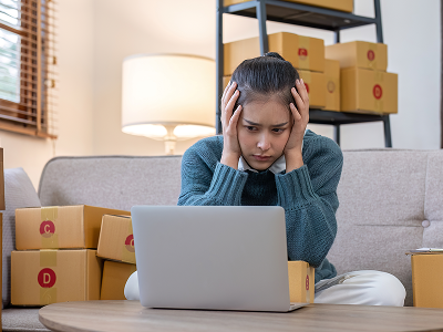 kobieta łapie się za głowę przed komputerem z paczkami dookoła